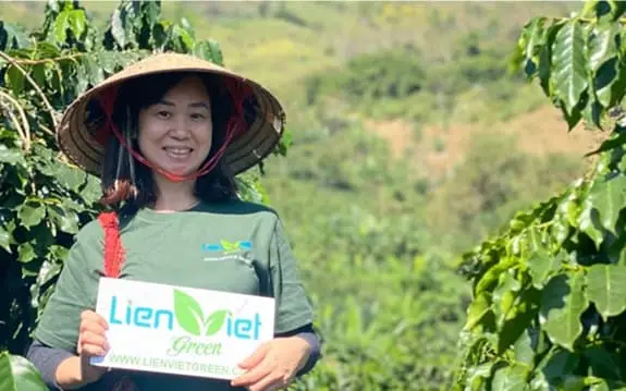 A woman in a conical hat holding a Lien Viet Green sign at a coffee farm