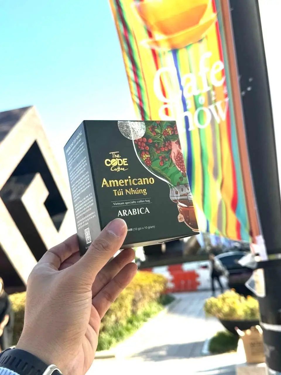 Hand holding The Code Coffee Americano Arabica drip bag box at Cafe Show