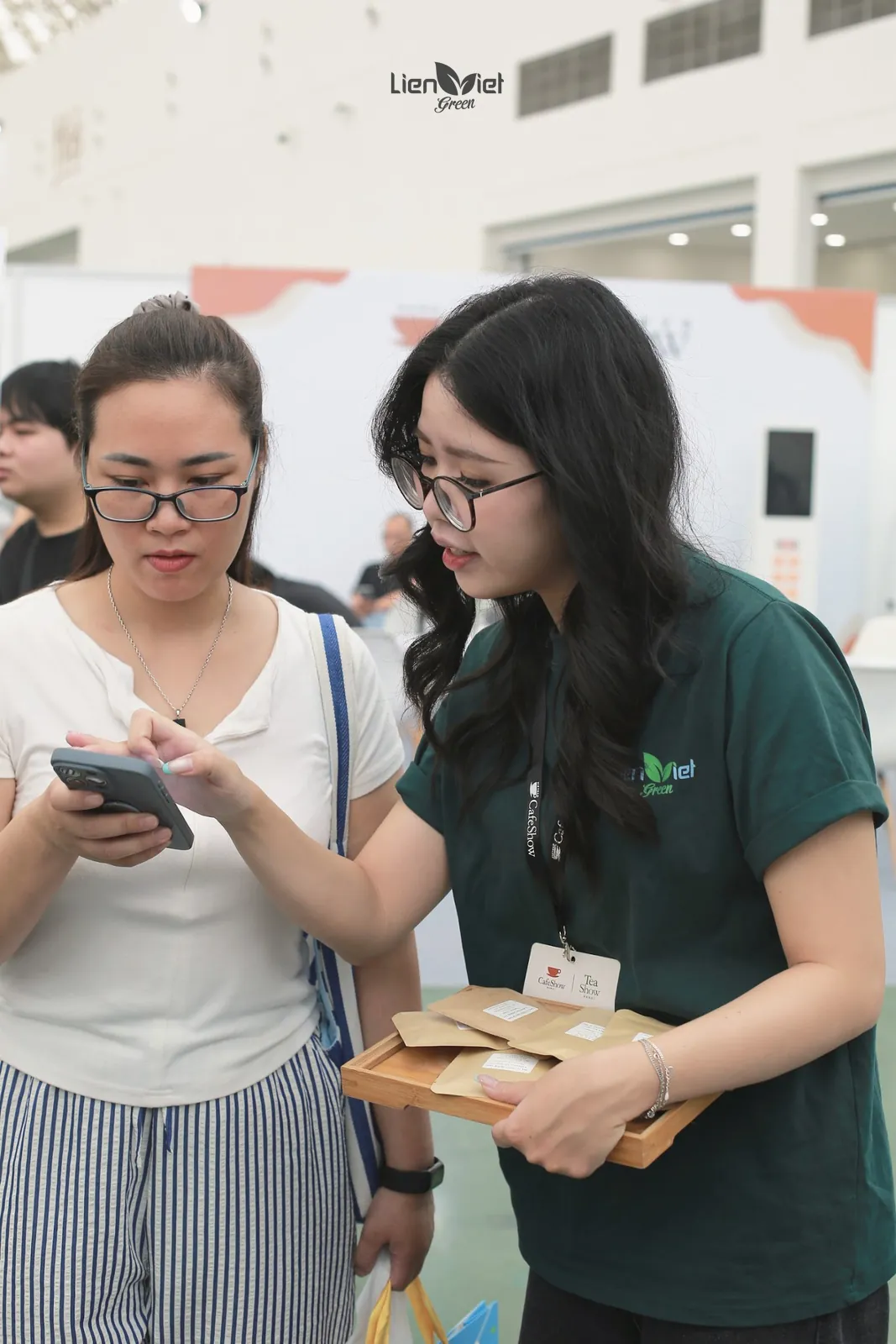 Nhân viên Liên Việt Green đeo thẻ Cafe Show tư vấn khách, tay cầm khay mẫu cà phê gói nhỏ.