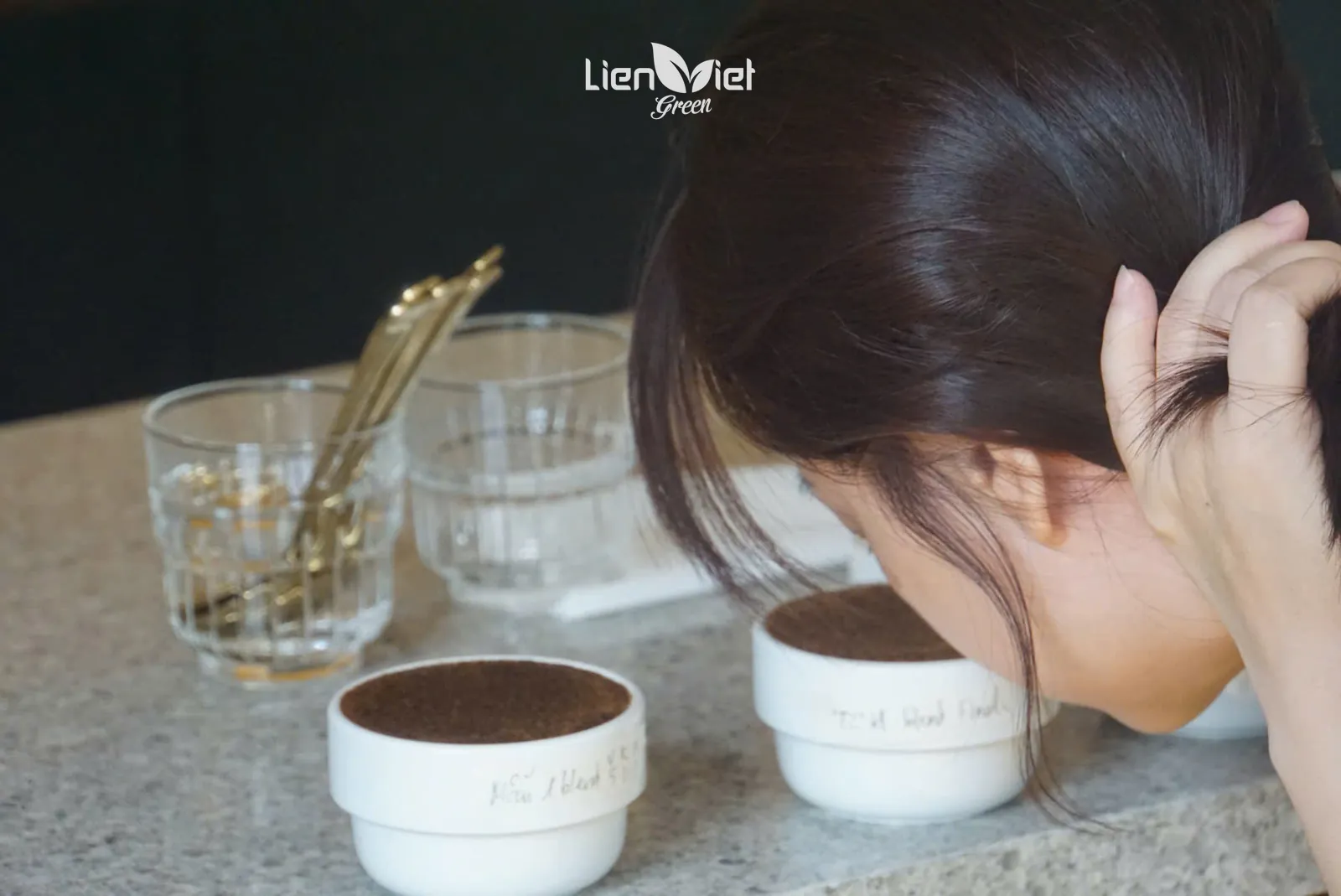 Chuyên viên cúi ngửi hương chén cà phê xay khi cupping kiểm tra chất lượng mẫu