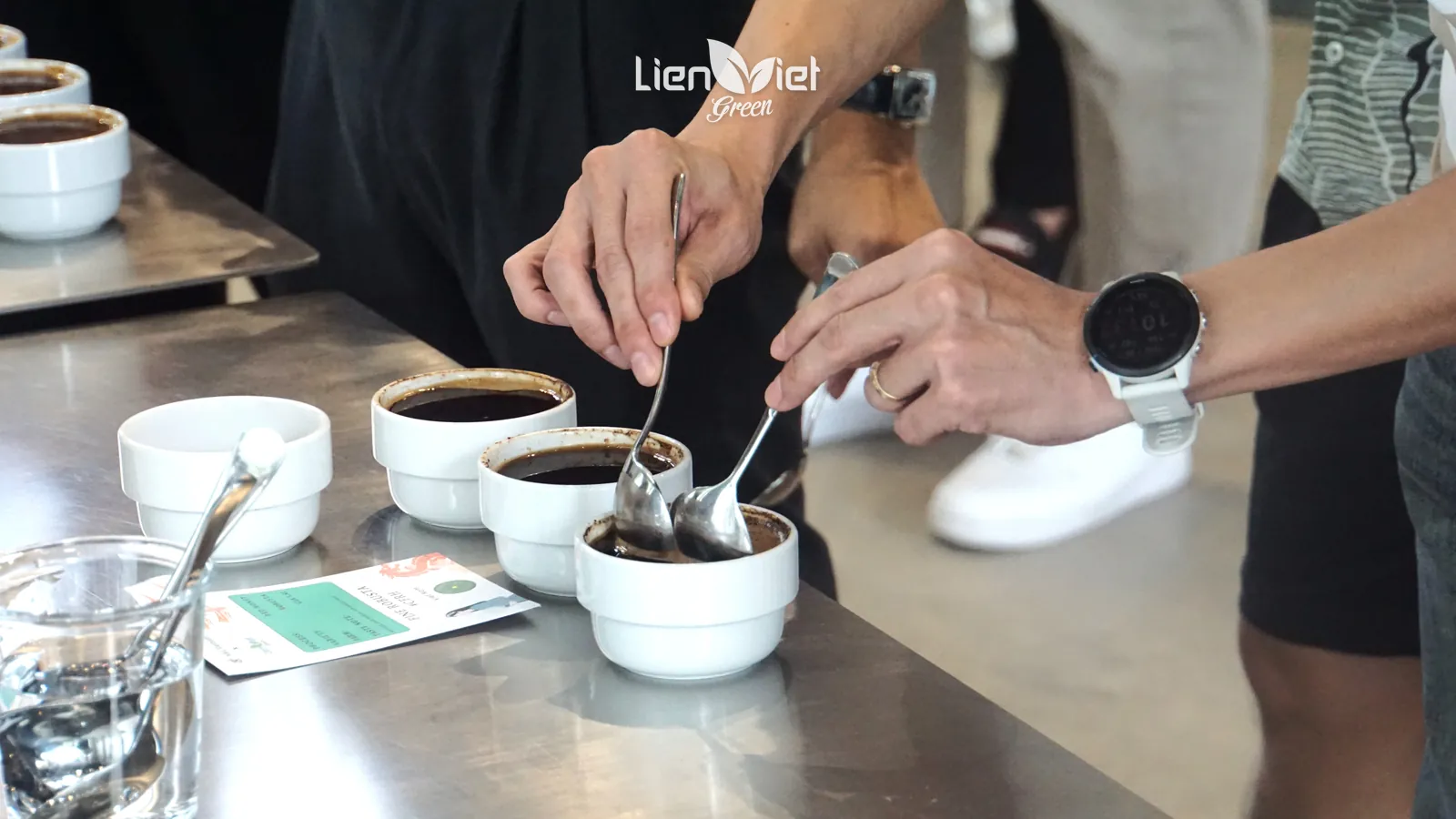 Close-up of a spoon breaking the coffee crust in a cupping bowl to smell the aroma