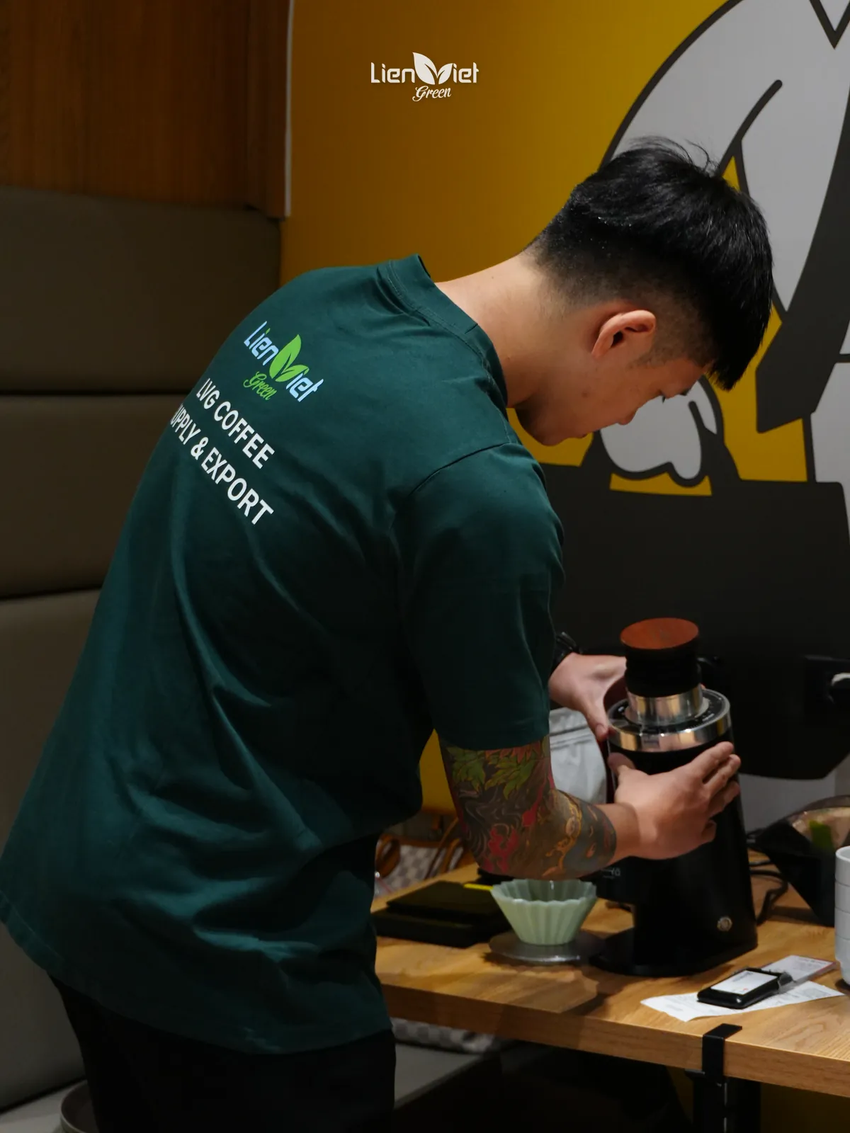 Barista in an LVG Coffee Supply & Export shirt grinding coffee before brewing at Flow & Brew #01