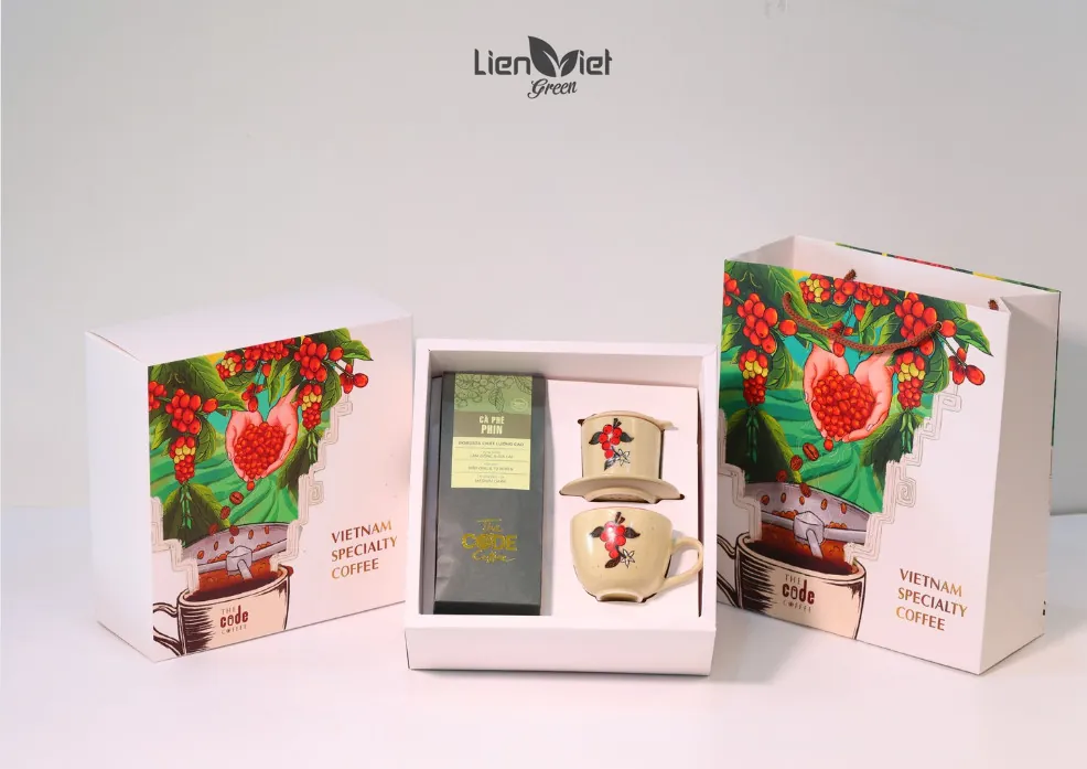 Gift box and matching bag with coffee-plant artwork, holding a phin coffee bag and ceramic phin set