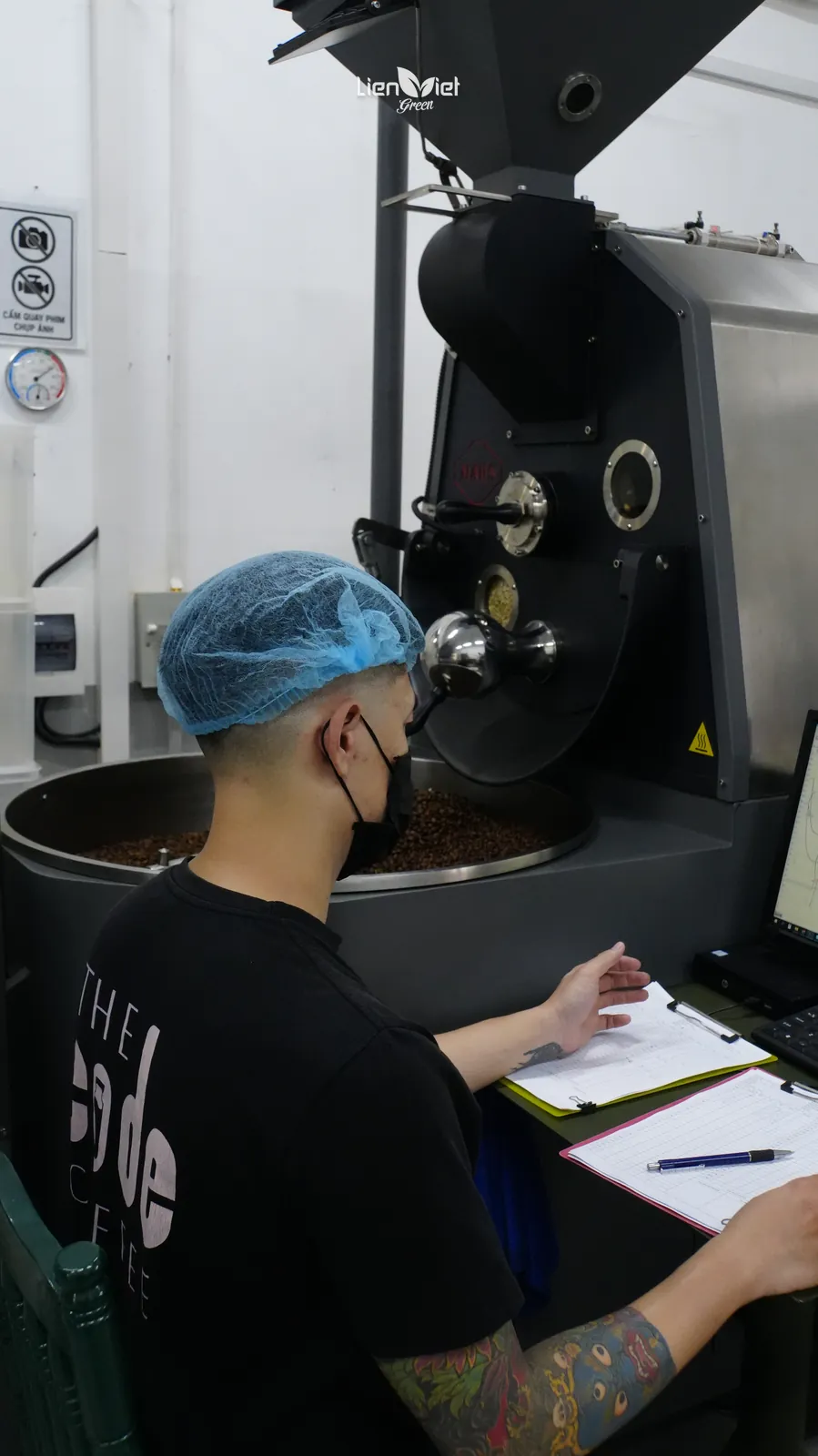 Kỹ thuật viên ghi chép dữ liệu hồ sơ rang bên máy rang và màn hình điều khiển tại xưởng Liên Việt Green